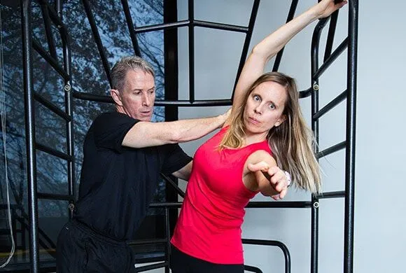 A male personal trainer helps a female client with her form during an exercise