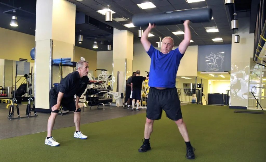 A male personal trainer coaches a male client in a blue t-shirt