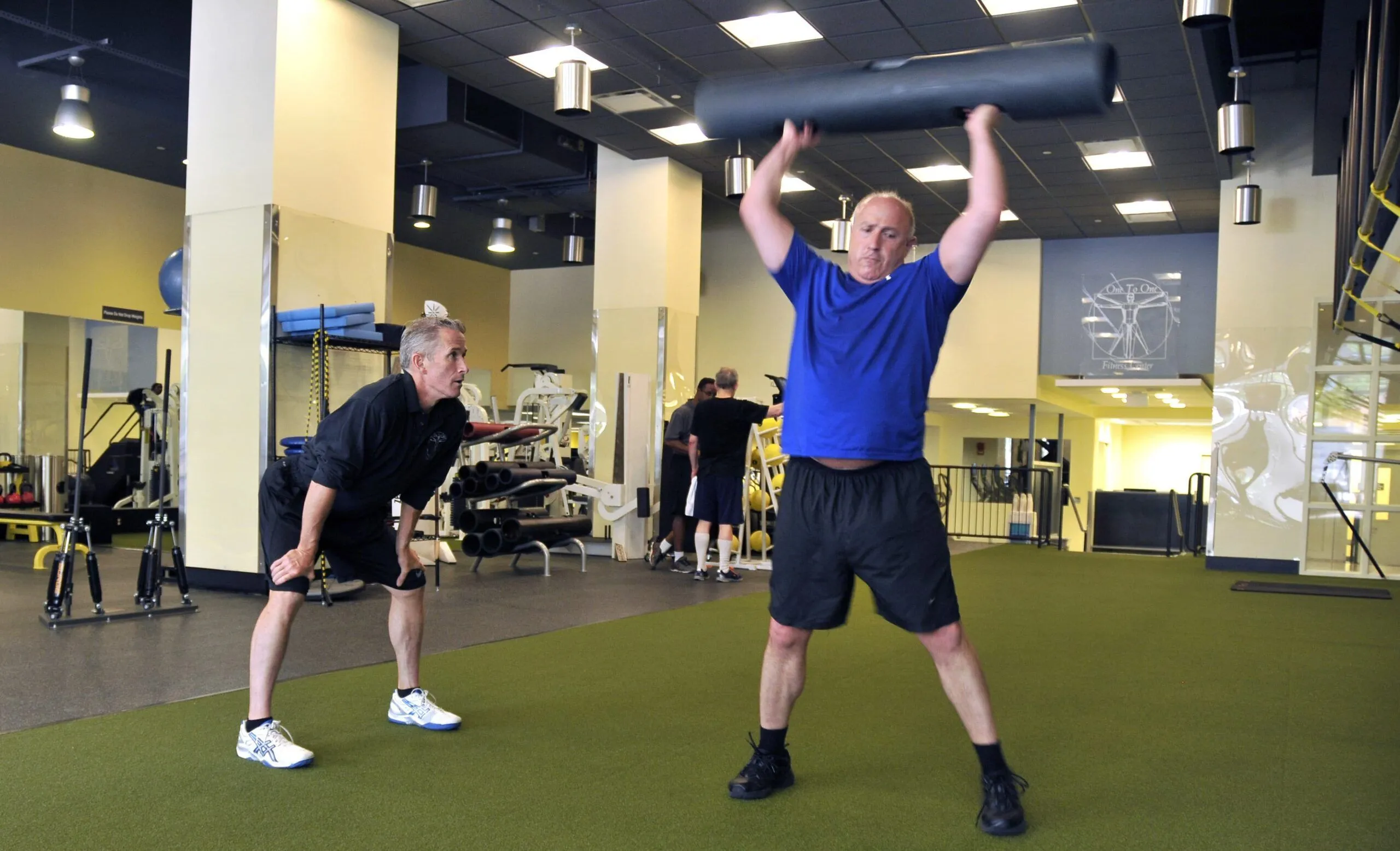 A male personal trainer coaches a male client in a blue t-shirt