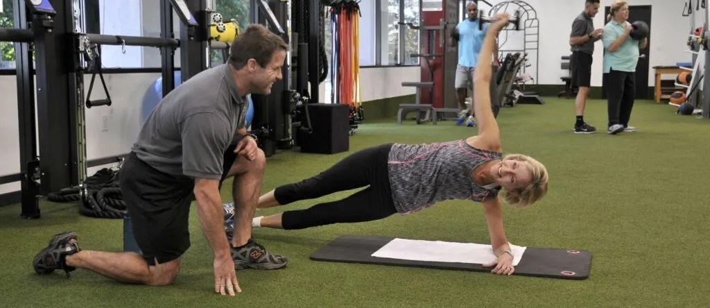A male personal trainer smiles while coaching a female client at 1TO1 Fitness