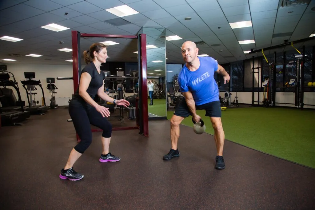 A female personal trainer coaches a male client through a weight exercise