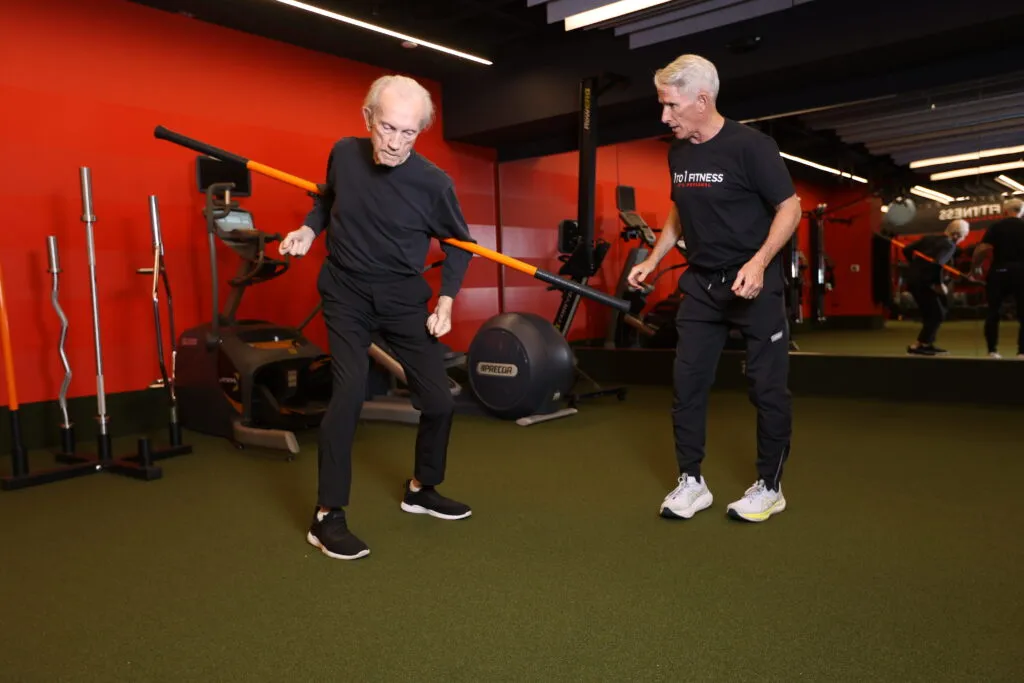 An older male client performs a mobility workout while a male personal trainer watches