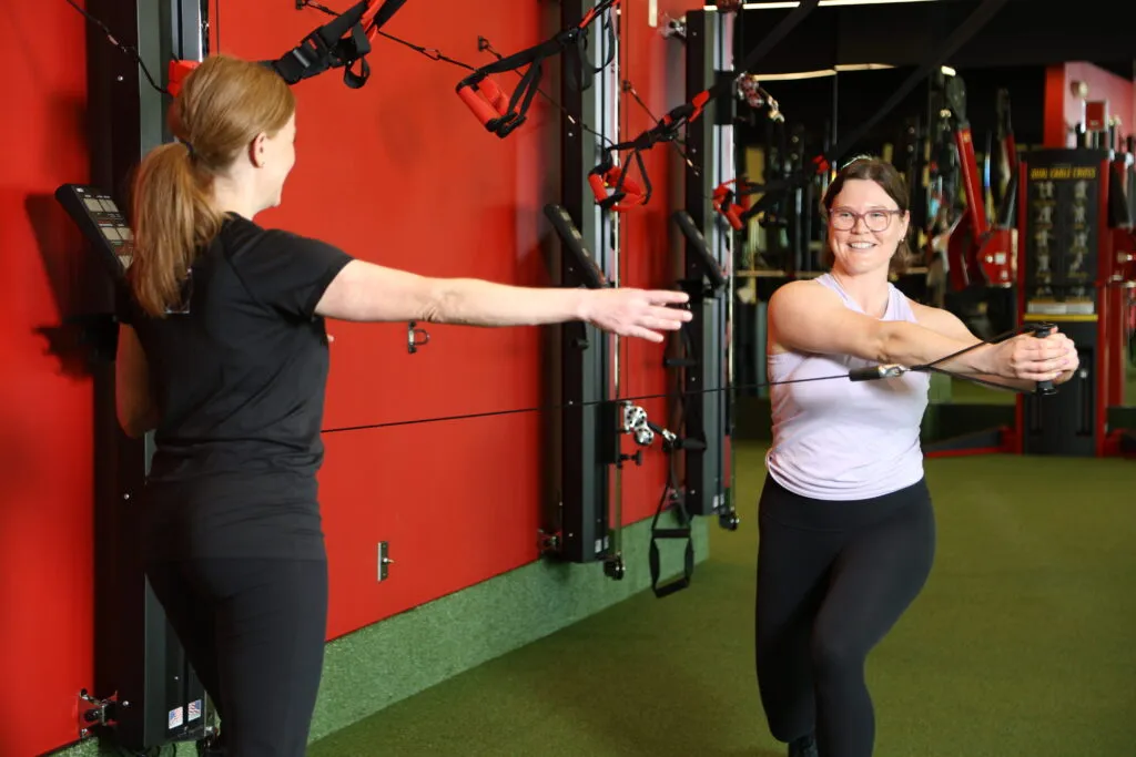 A female client smiles while being coached through a TRX workout
