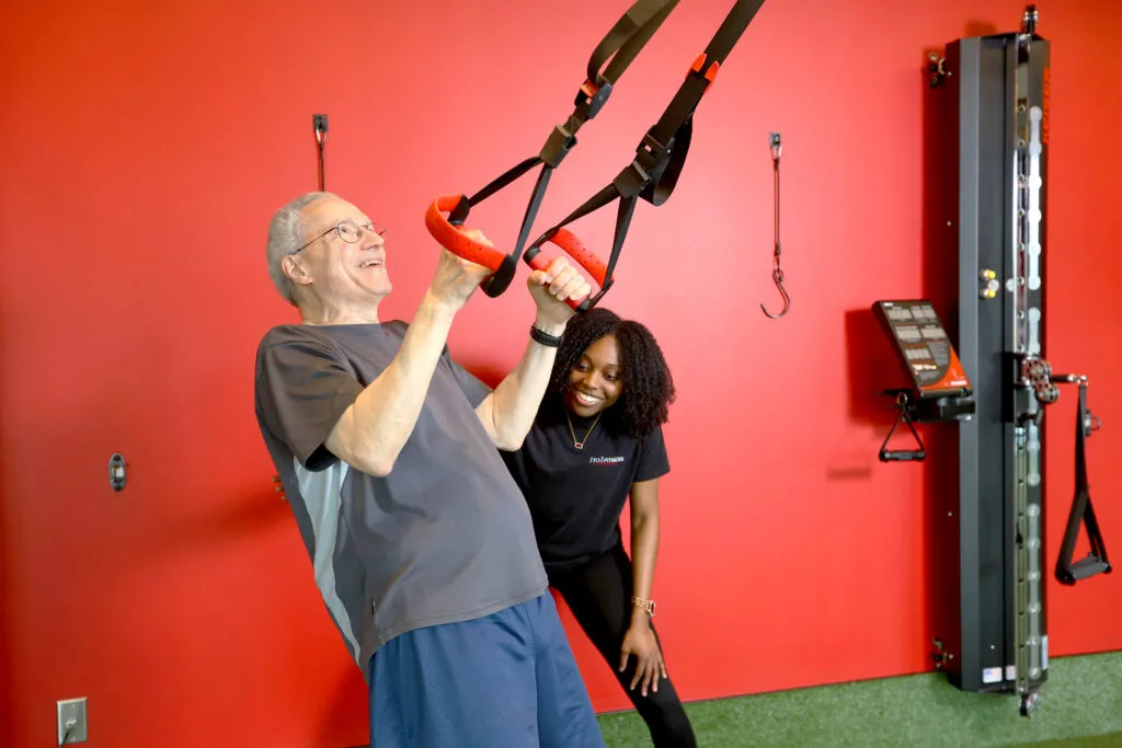A female personal trainer smiles while helping a male client work through an exercise