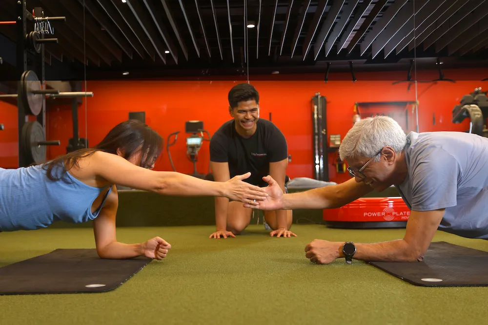 Personal trainer guiding couple through partner plank exercise in private personal training gym