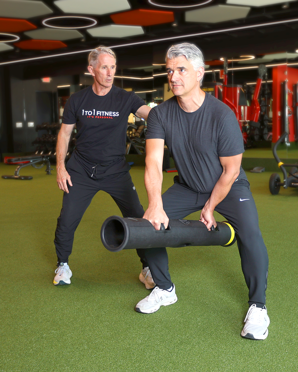Personal trainer coaching client performing weighted bar lunge exercise at 1to1 fitness