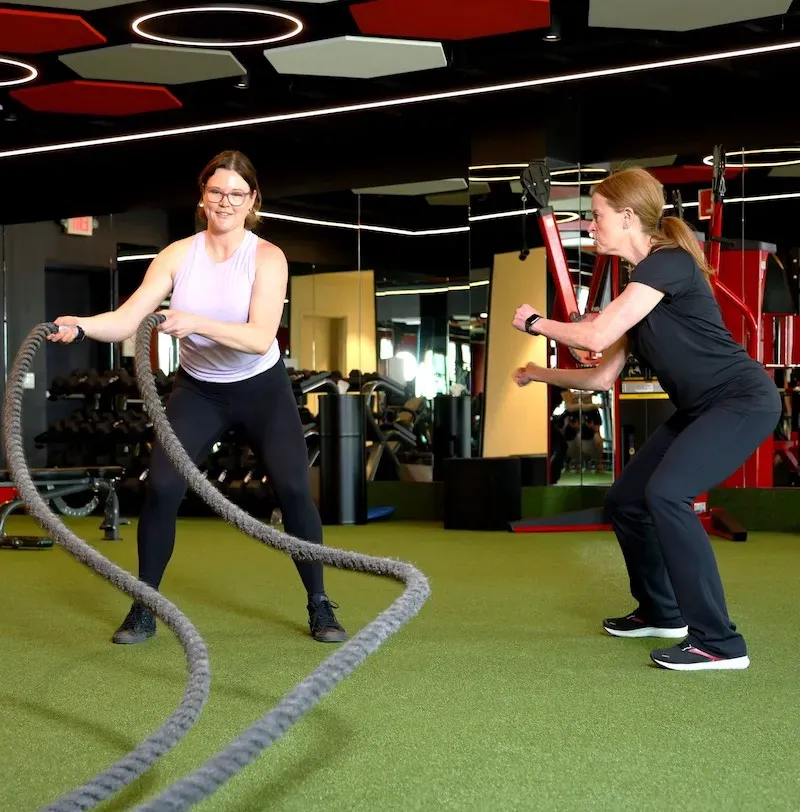 A female personal trainer coaches a female client through a ropes workout