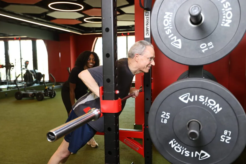 A male personal training client smiles while leaning against a weight bar