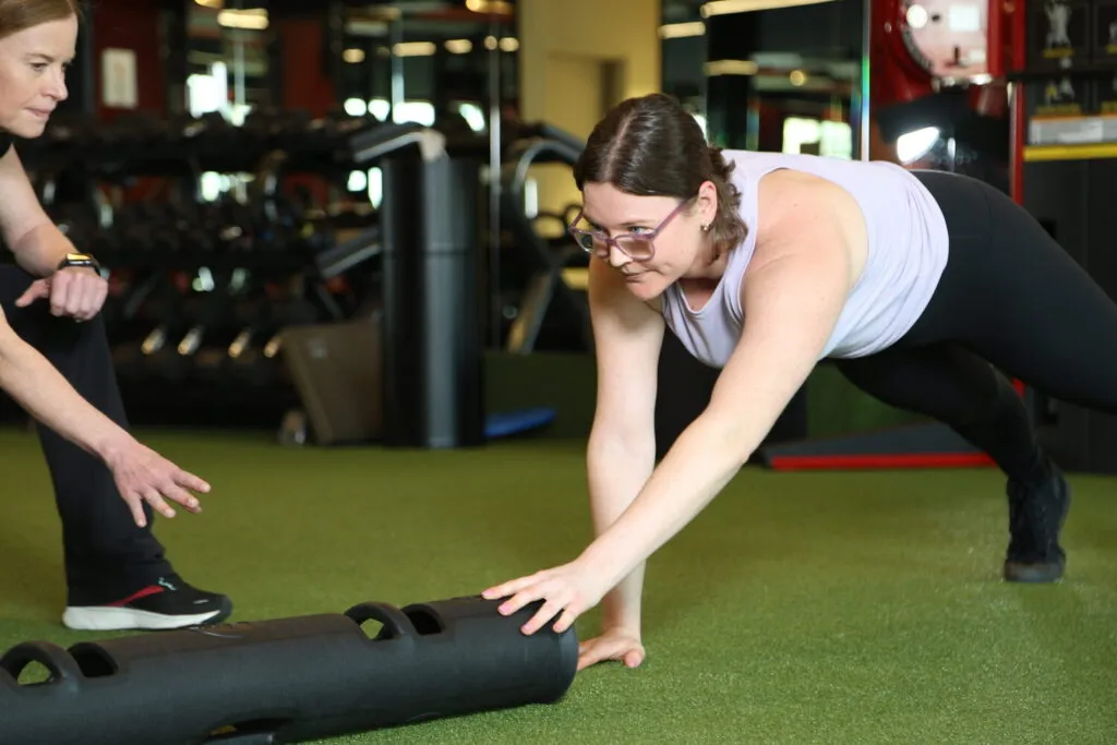 A female personal trainer smiles while watching a female client work through an exercise