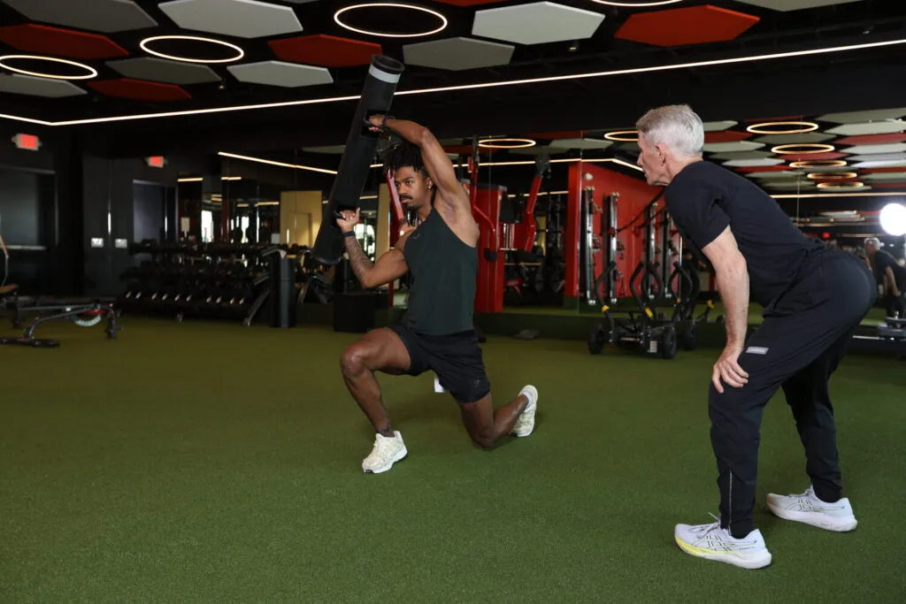 A male personal training client smiles while being instructed by a male personal trainer