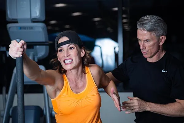 A male personal trainer coaches a female client through a cardio workout
