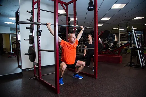 A male personal trainer coaches a male client through an overhead weight press